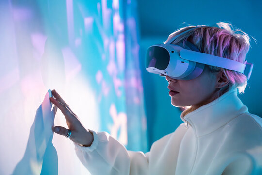 Futuristic woman in VR headset touching glowing digital wall