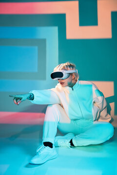 Futuristic woman in VR headset pointing in neon studio set