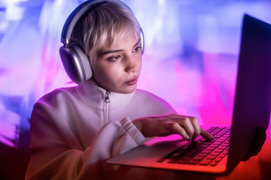 Futuristic woman using laptop with headphones in neon light