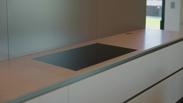 The kitchen countertop is sleek and modern, induction cooktop blends seamlessly with surface, glossy handle-less drawers below add clean look, design feels minimal