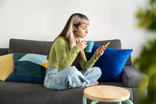 Young woman on sofa with coffee using smartphone at home
