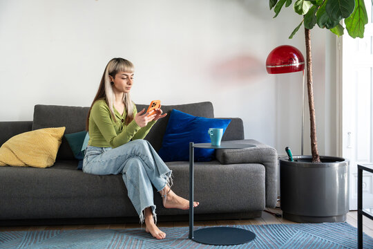 Young woman using smartphone on sofa in modern living room