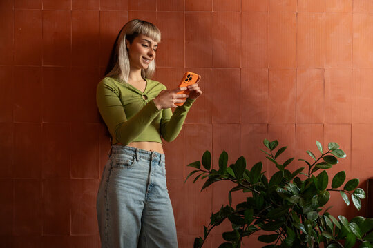 Young woman using smartphone by terracotta wall at home