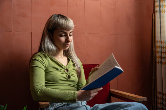 Young woman reading a book on a chair in warm light