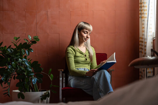 Woman reading a book in cozy room with indoor plant