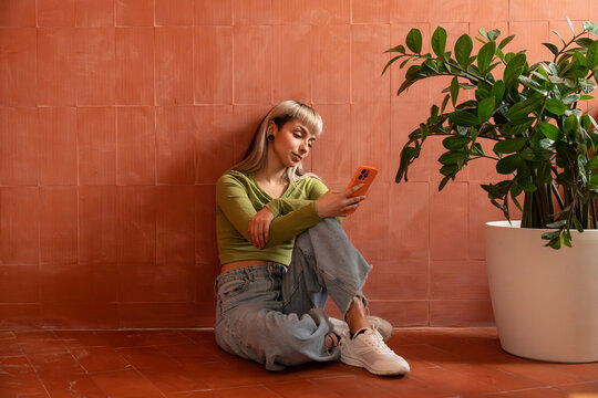 Young woman using smartphone on terracotta floor by plant