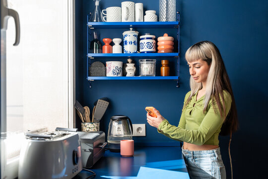 Woman using smartphone in modern blue kitchen at home