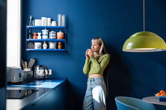 Young woman enjoying coffee in a modern blue kitchen at home