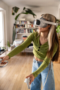 Young woman playing virtual reality game at home with headset