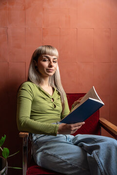 Portrait of woman with book on a red chair looking at camera