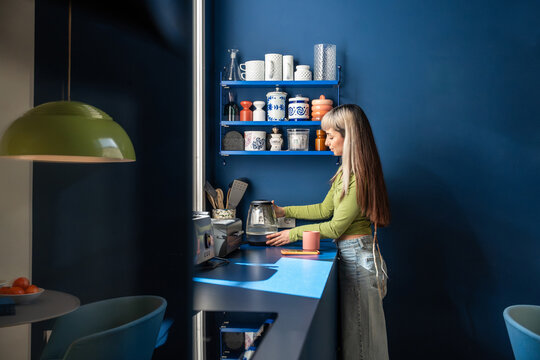 Woman preparing tea at home kitchen counter in blue room