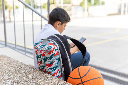 Boy sitting with backpack and basketball at school