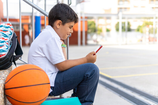Young boy sitting on steps using phone at schoolyard