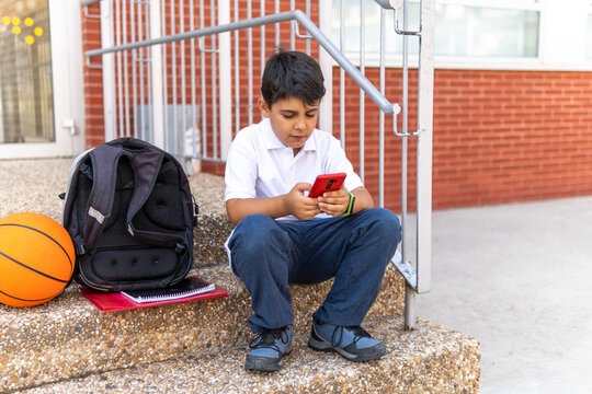 Boy sitting on school steps with smartphone