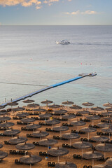 Fototapeta premium Luxury resort beach in Sharm El Sheikh, Egypt, featuring rows of straw umbrellas, a long floating pier, and a white yacht on the calm Red Sea at sunset.