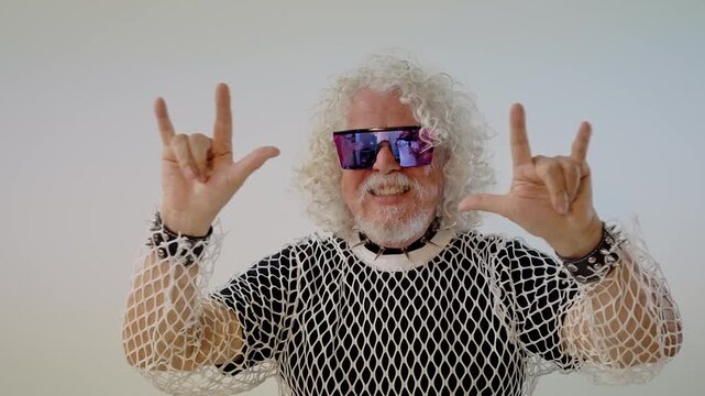 Charismatic senior man with curly hair and sunglasses gesturing the sign of the horns, celebrating rock and roll culture with a rebellious attitude, isolated on a white background studio setting