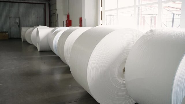 Large white rolls of polypropylene fabric in a factory warehouse