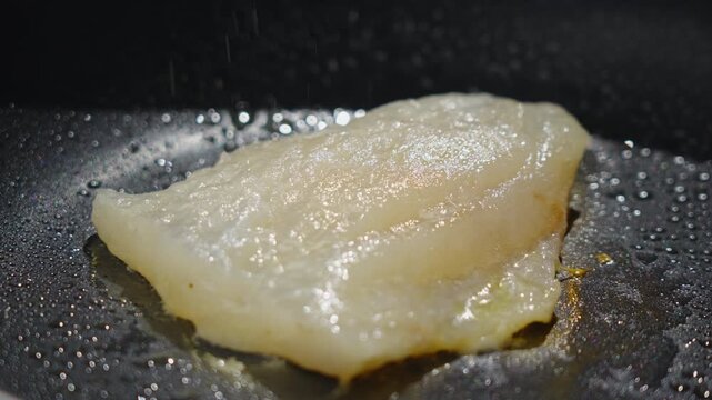 Frying white fish fillets. Frying hake fillets in a hot pan Gentle low heat pan cooking of white fish fillet, closeup of subtle bubbling and translucent center slowly turning