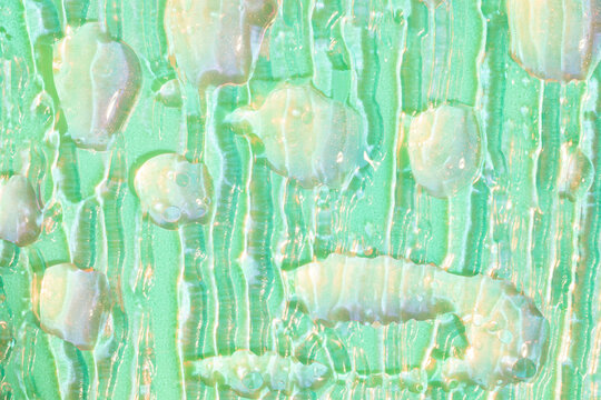 Cosmetic serum drops in neon light on textured glass backdrop