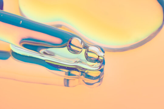 Cosmetic serum dropper in neon light with glossy texture