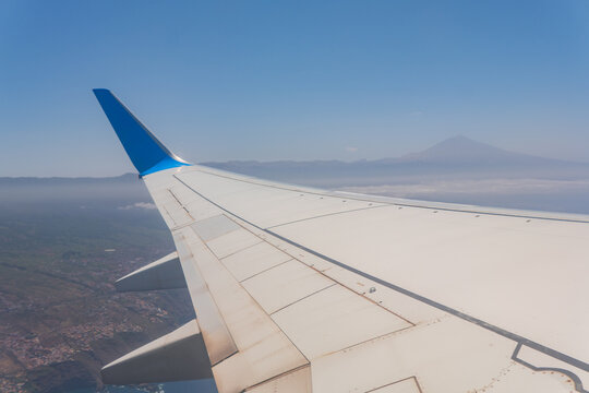 Airplane wing view above clouds with distant mountain