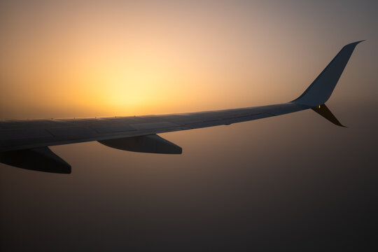 Airplane wing silhouette against sunrise above cloud layer