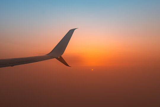Airplane wing silhouette above clouds at glowing sunset