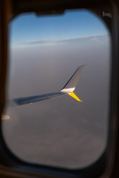 Airplane wing seen through window above clouds at altitude