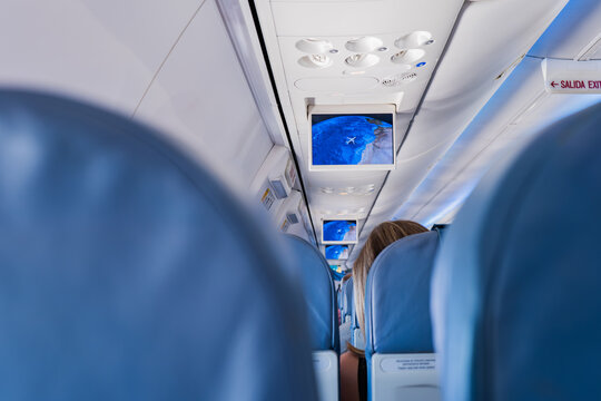 Airplane cabin aisle view with overhead screens during flight