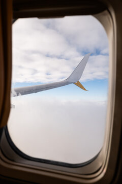 Airplane window view of wing above clouds in flight