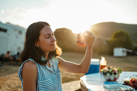 Woman enjoying grapes at summer picnic in golden sunset