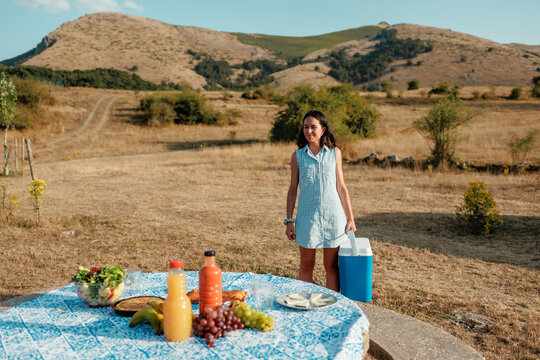 Woman setting up summer picnic with cooler in countryside