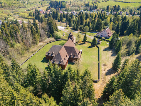 Aerial view of the Wooden Articular Church of Svaty Kriz surrounded by a wooden fence and lush green forest in Svaty Kriz, Zilinsky kraj, Slovakia.