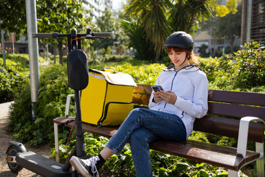 Woman delivery rider checking smartphone beside scooter