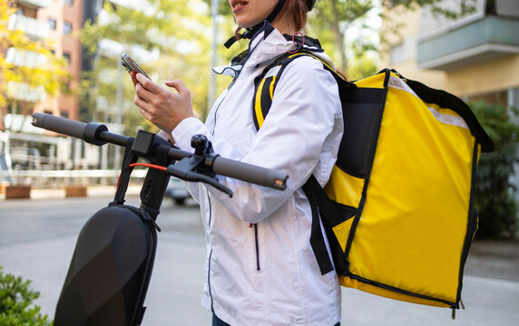 Female food delivery rider checking phone by scooter