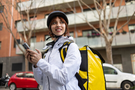 Female food delivery rider checking phone on city street