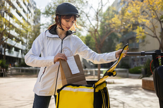 Female courier loading takeaway order onto e-scooter