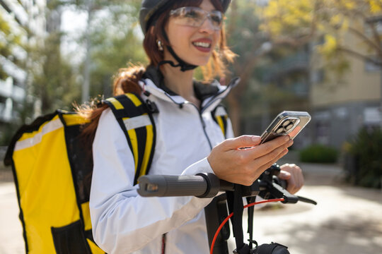 Female food delivery rider checking smartphone by scooter