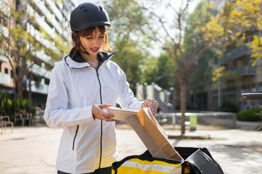 Female food delivery rider checking takeout on street