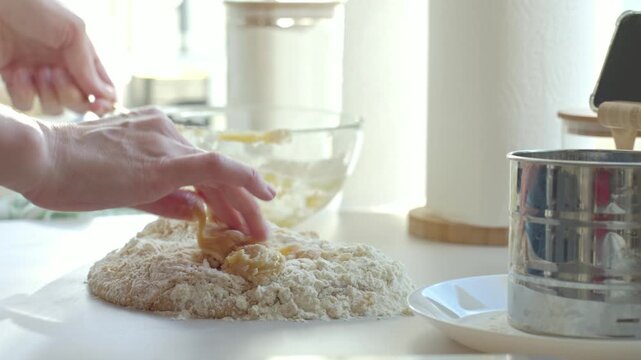 Hands work sticky dough with flour on kitchen counter beside sifter and bowl