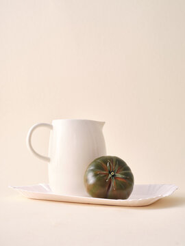 Minimalist still life with white pitcher and ripe tomato