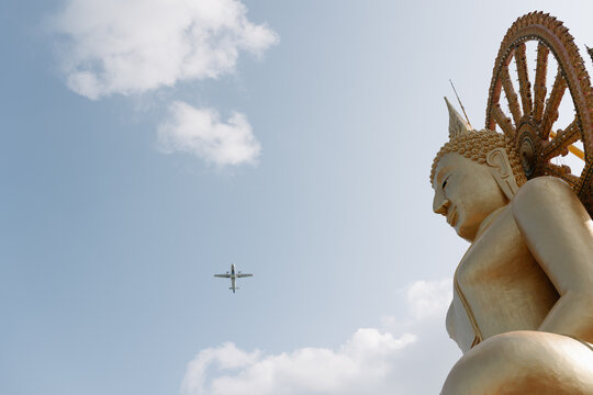Golden Buddha statue at Thai temple with plane overhead