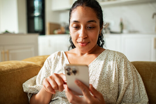 Smiling woman using smartphone on sofa at home