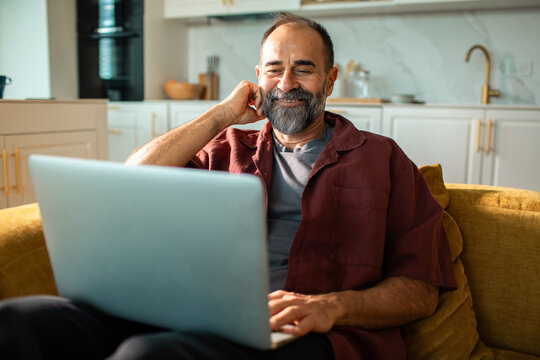 Middle-aged man using laptop on sofa in home kitchen