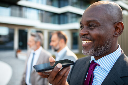 Smiling businessman using voice assistant outdoors with colleagues