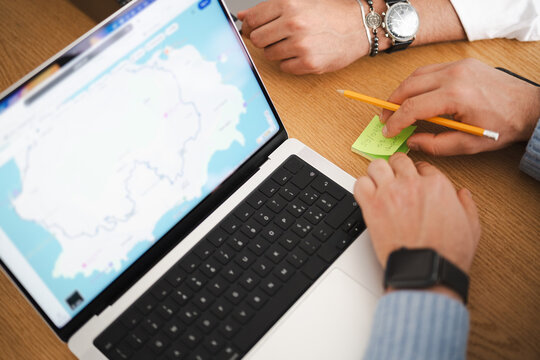 Two people collaborate on a project, using a laptop displaying a map and a sticky note with handwritten details.