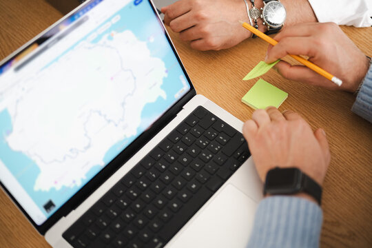 Two people collaborate on a project, using a laptop displaying a map and sticky notes for planning.