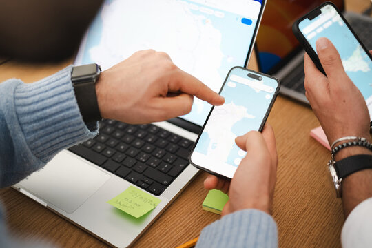 Two people are using their phones and a laptop to plan a trip, looking at maps and destinations on their devices.