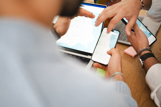A group of people collaborate, using a laptop and smartphone to view a map and plan their next destination.