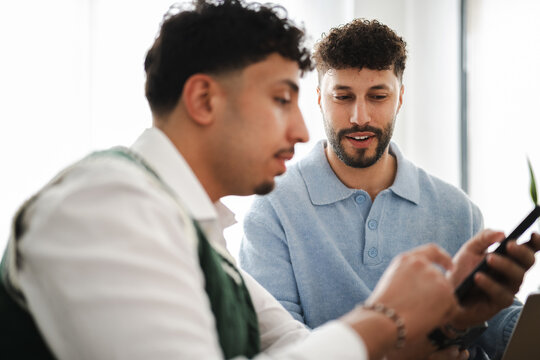Two men are collaborating on a project, one holding a mobile device and the other looking on attentively.